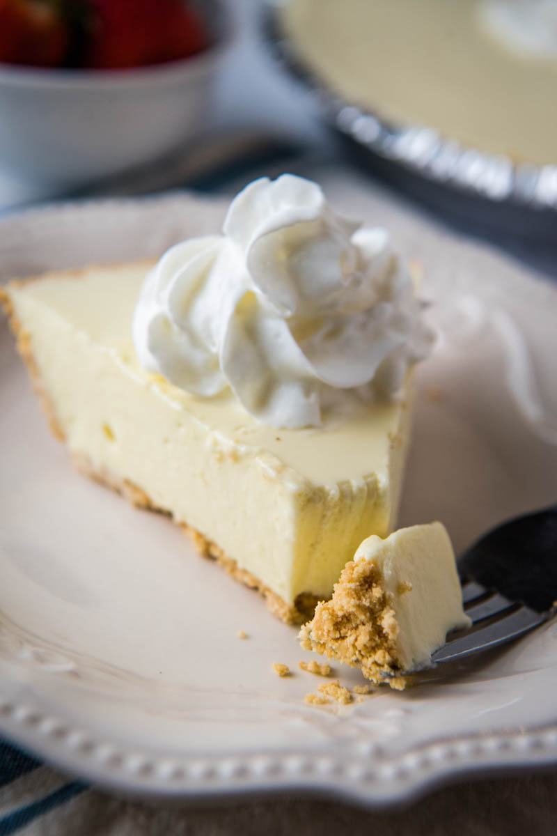 slice of Jello cheesecake topped with whipped cream on ivory plate with forked bite