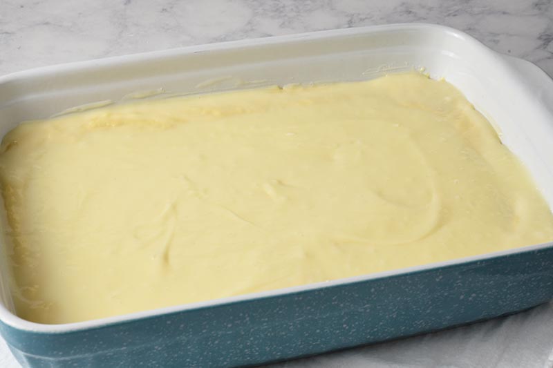 gooey butter cake filling topping the cake mix crust in a blue baking dish