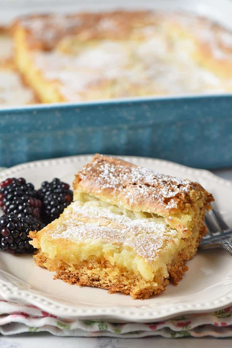 slice of gooey butter cake with blackberries on an ivory plate with fork