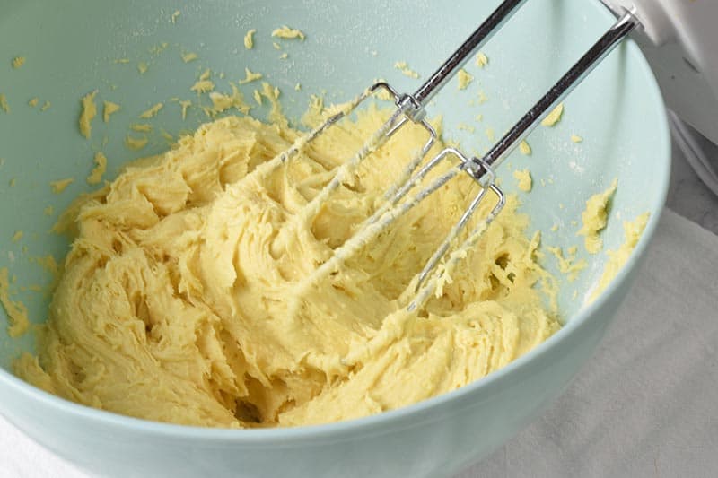 mixing ingredients for cake mix gooey butter cake crust in blue mixing bowl with hand mixer