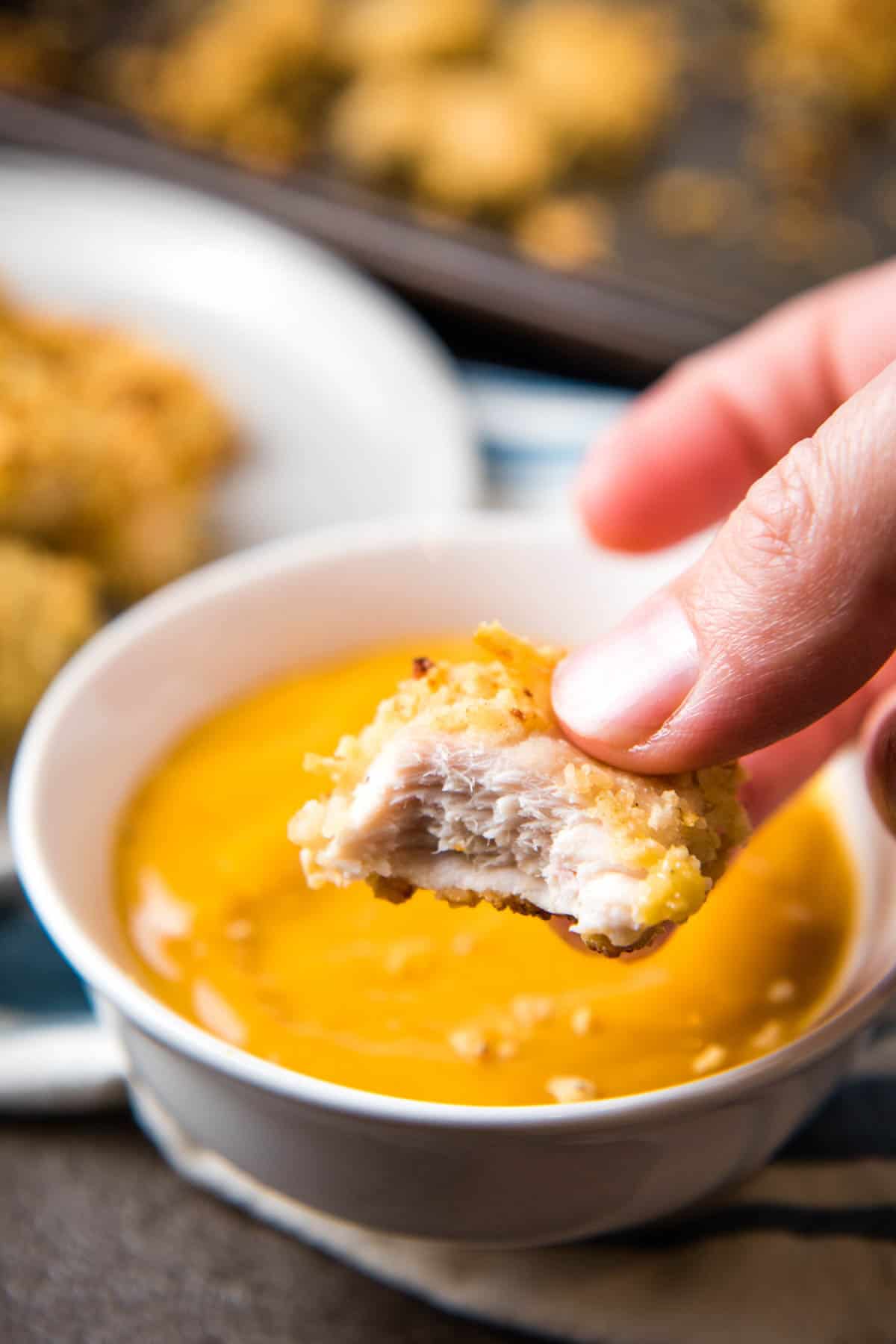fingers holding chicken Pringler with bite taken out over white bowl with chicken dipping sauce