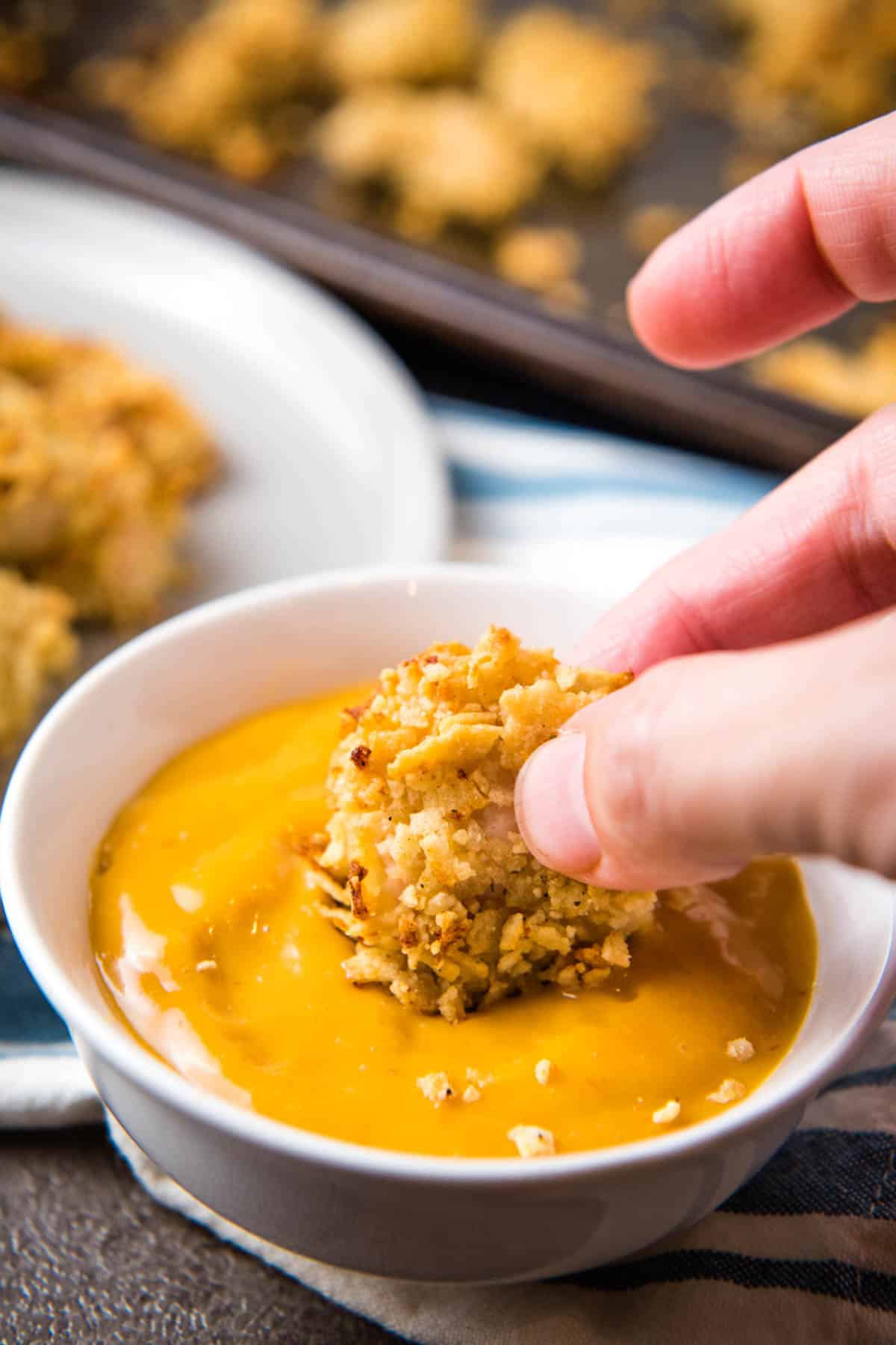 fingers dipping Pringles coated chicken nugget in chicken dipping sauce in white bowl