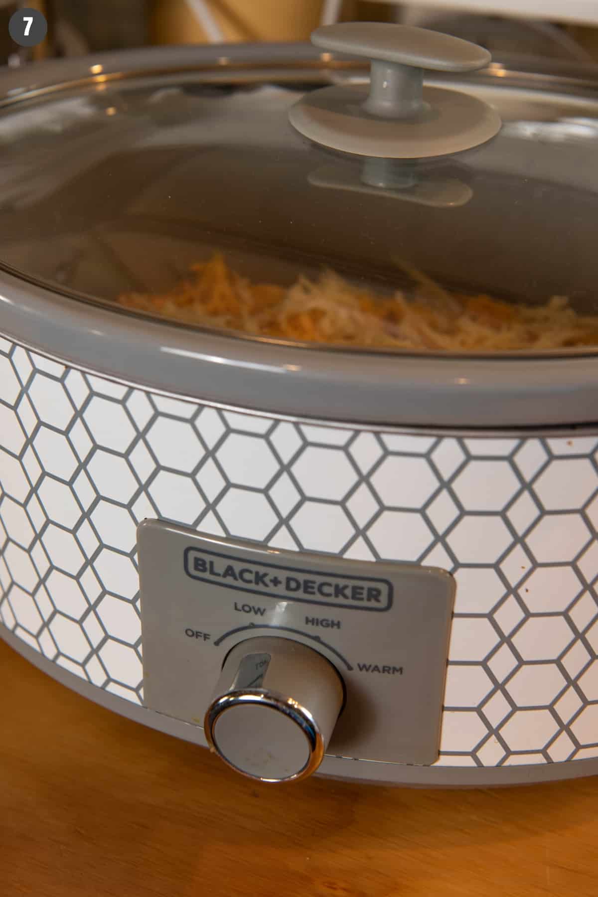 cooking slow cooker chicken enchilada casserole in Black + Decker slow cooker on low on wood countertop