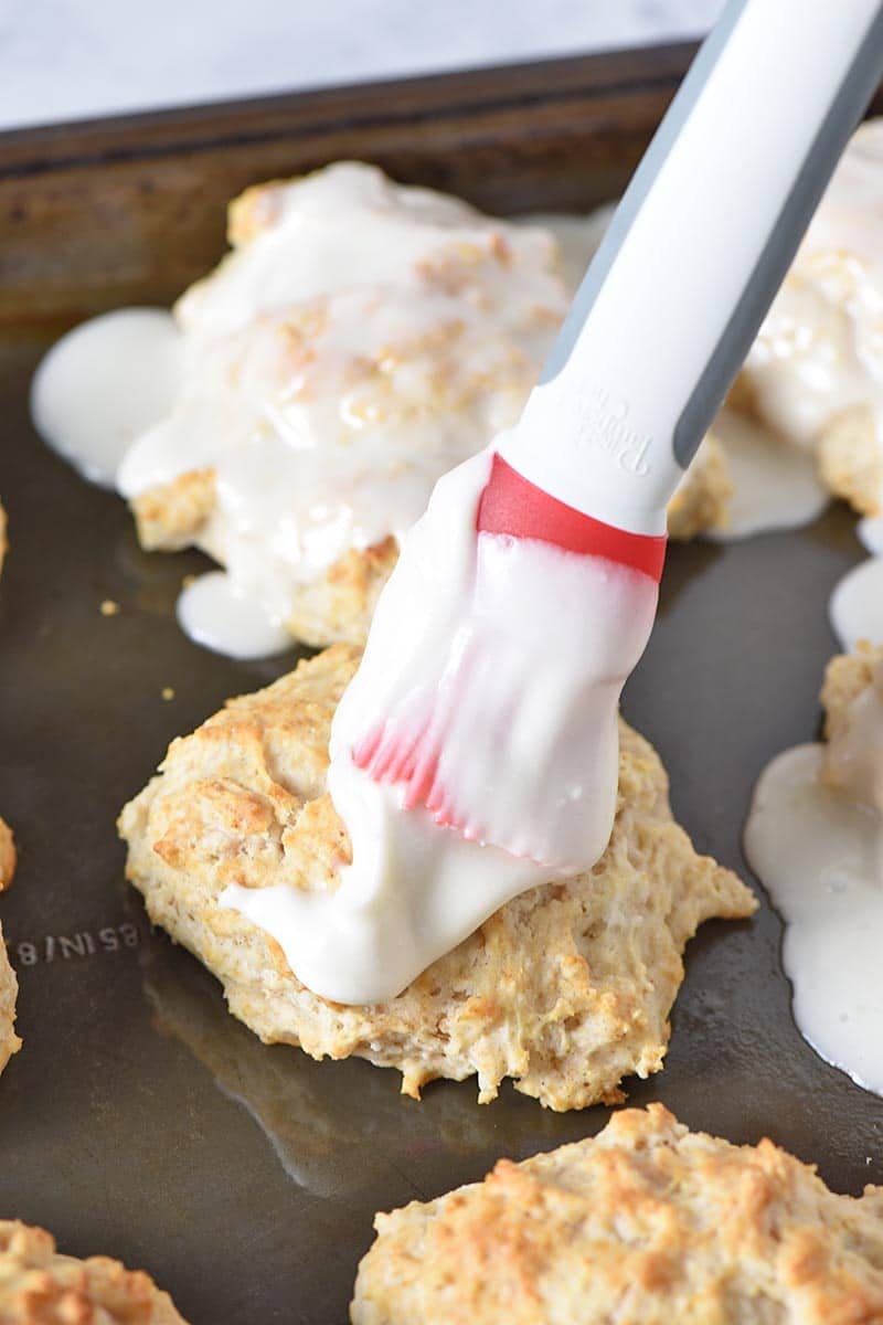 brushing Bisquick cinnamon biscuits with powdered sugar glaze on baking sheet