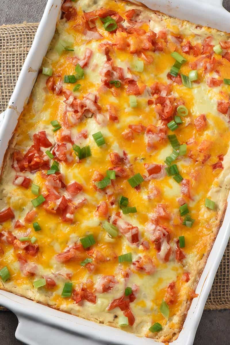 homemade chicken enchiladas with tomatoes and green onions in a white baking dish, baked and ready to eat