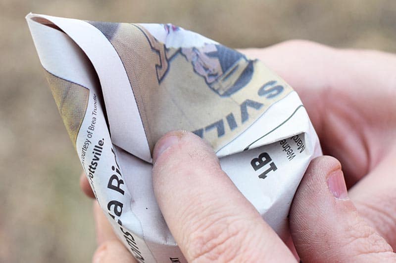 folding newspaper end over tin can for seed starter pot