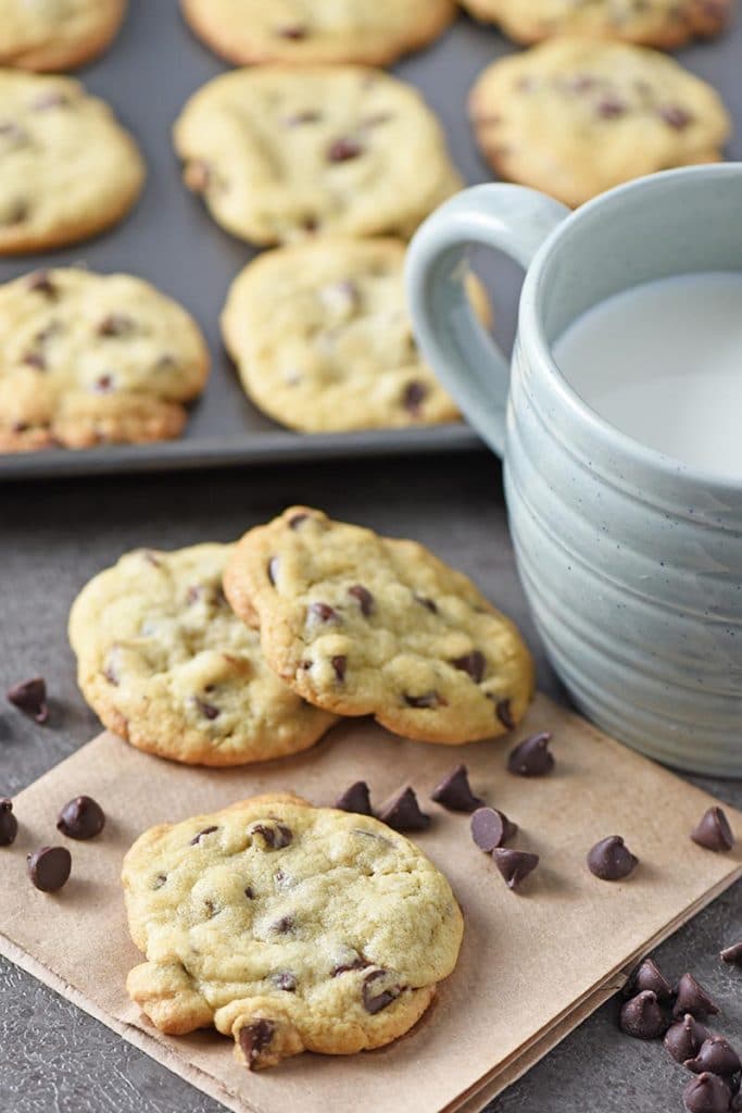 chewy chocolate chip cookies on brown paper bag with chocolate chips and cold milk