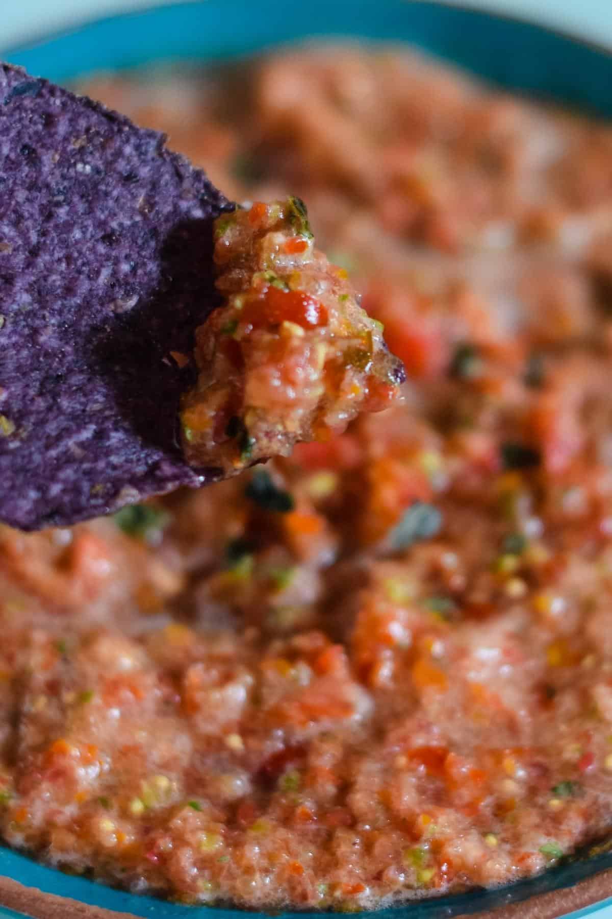 basil salsa on blue tortilla chip over blue bowl of salsa