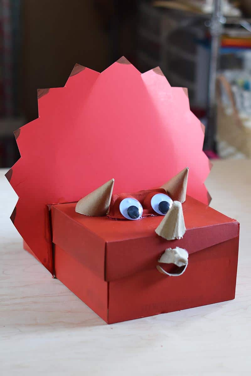 Triceratops homemade dinosaur Valentine box painted red with eyes and horns, sitting on a table