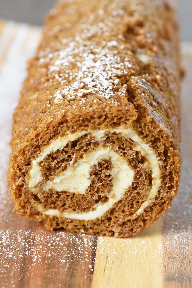 pumpkin roll sprinkled with powdered sugar on a wooden cutting board