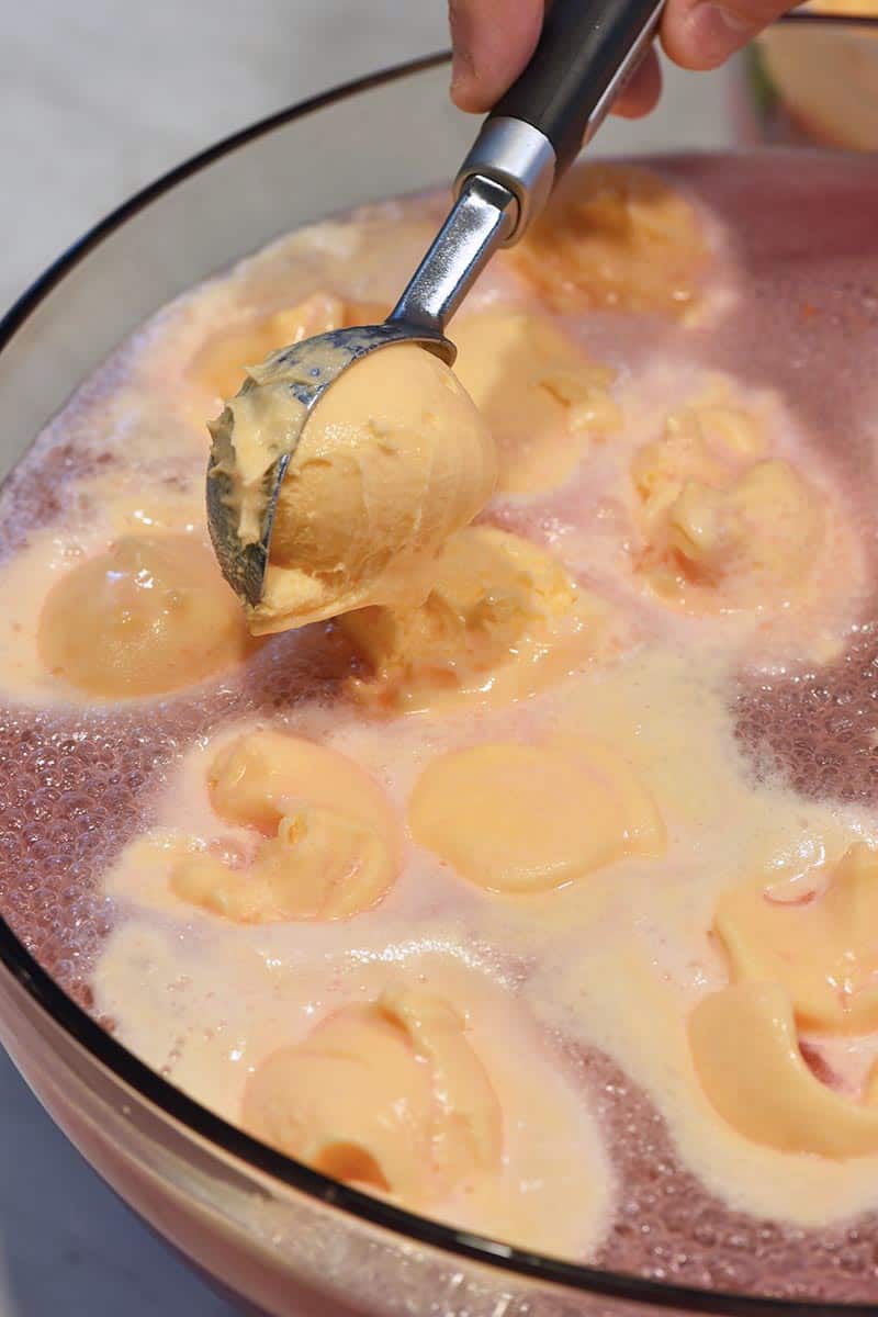 scooping orange sherbet while making orange sherbet punch in punch bowl