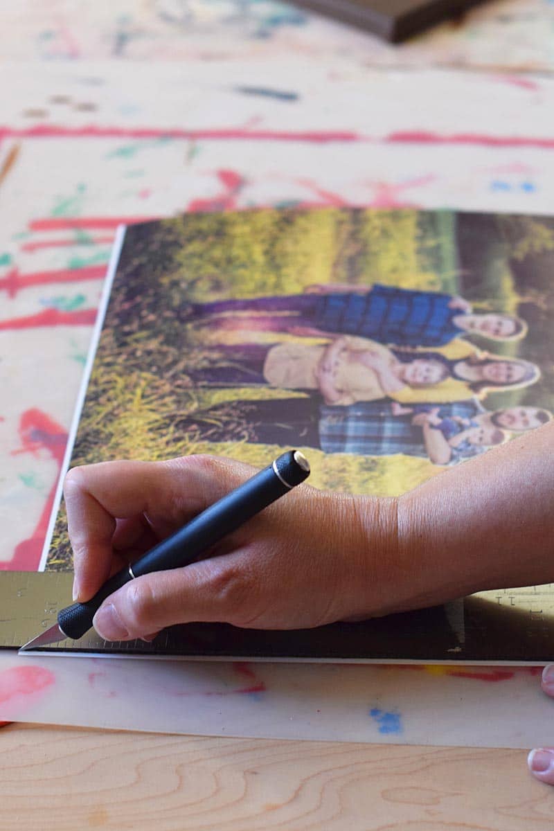 preparing to make a photo canvas by trimming the white edges off photos with a craft knife on a craft board