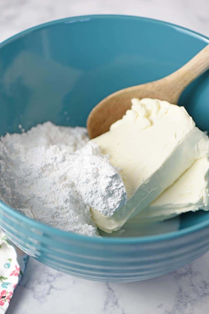 mixing bowl and wooden spoon with cream cheese, powdered sugar, and milk for no bake strawberry cream pie recipe