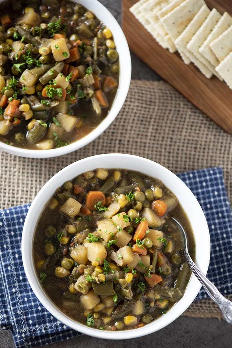 white bowls of chunky vegetable soup with crackers on a wooden cutting board