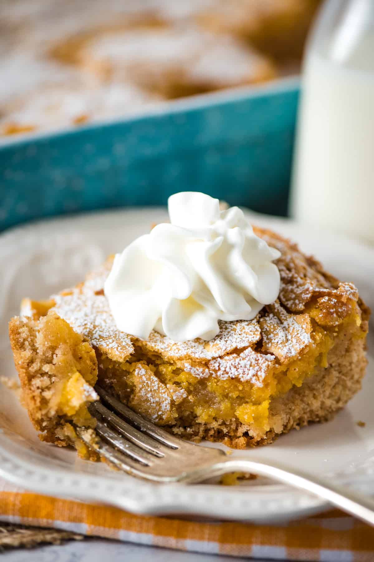 fork with bite and slice of gooey butter pumpkin cake topped with whipped cream on white plate