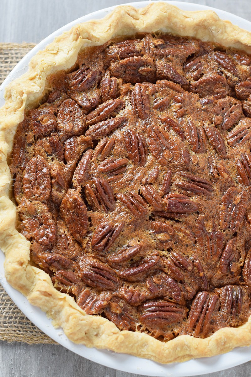 whole southern pecan pie, baked in white pie plate, sitting on wood countertop
