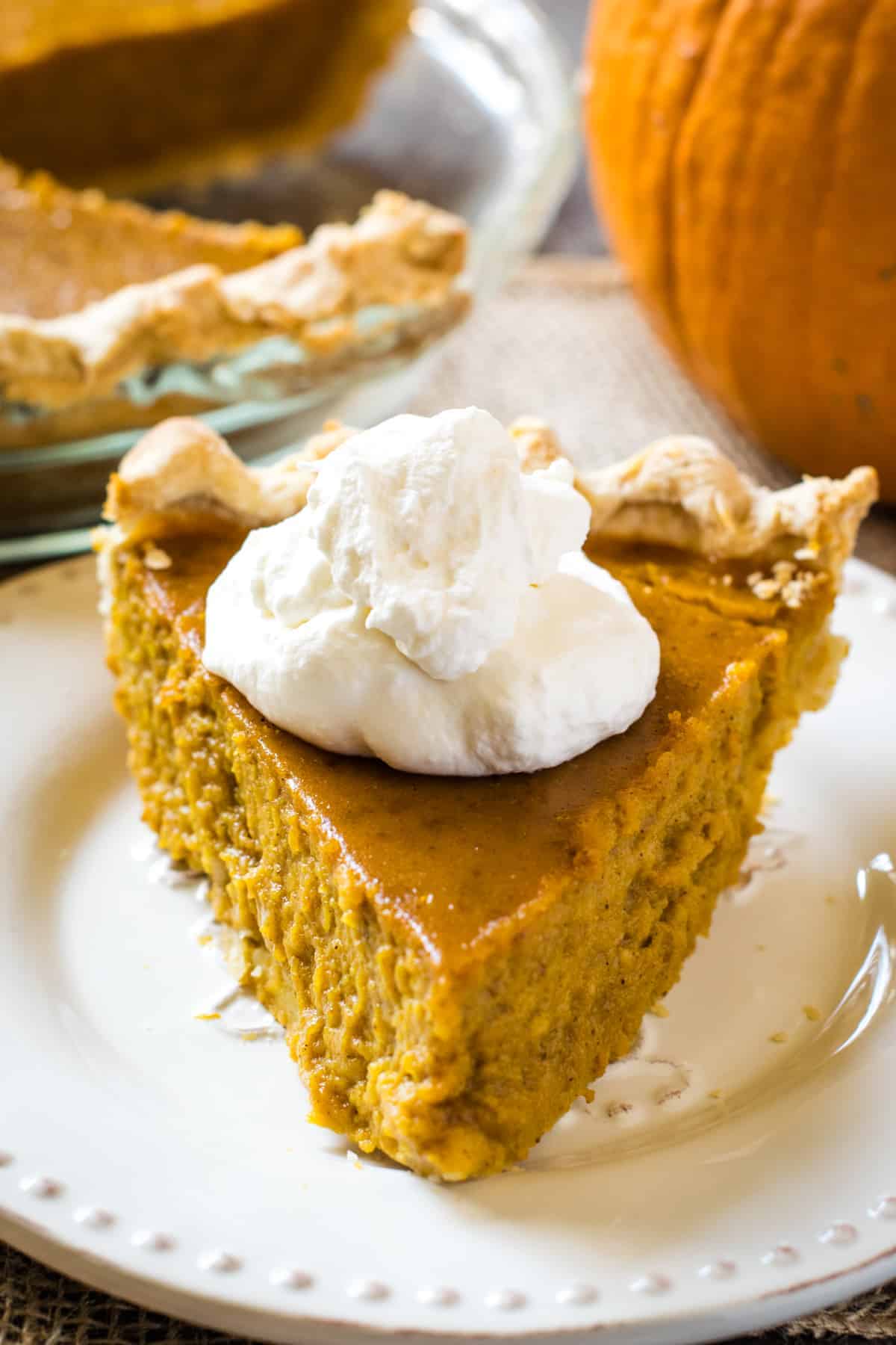 slice of old-fashioned pumpkin pie from scratch, topped with whipped cream, on white plate