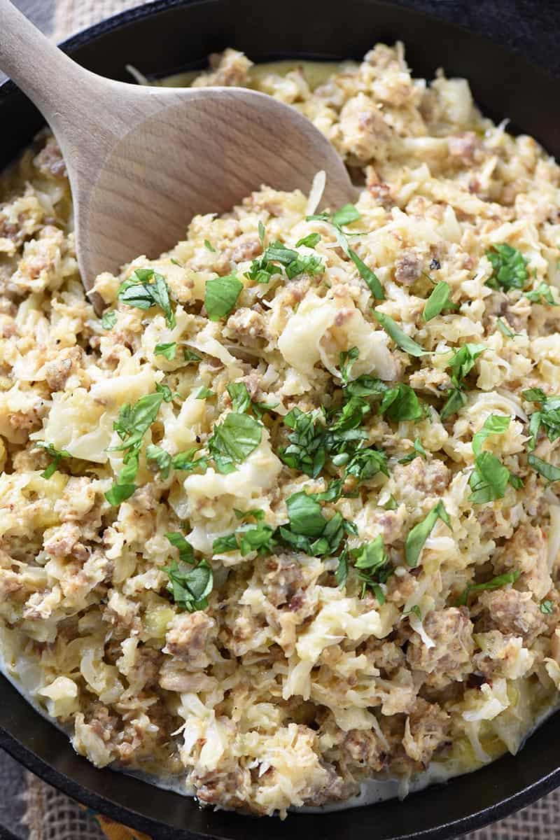 sausage and chicken casserole with wooden spoon in black cast iron skillet