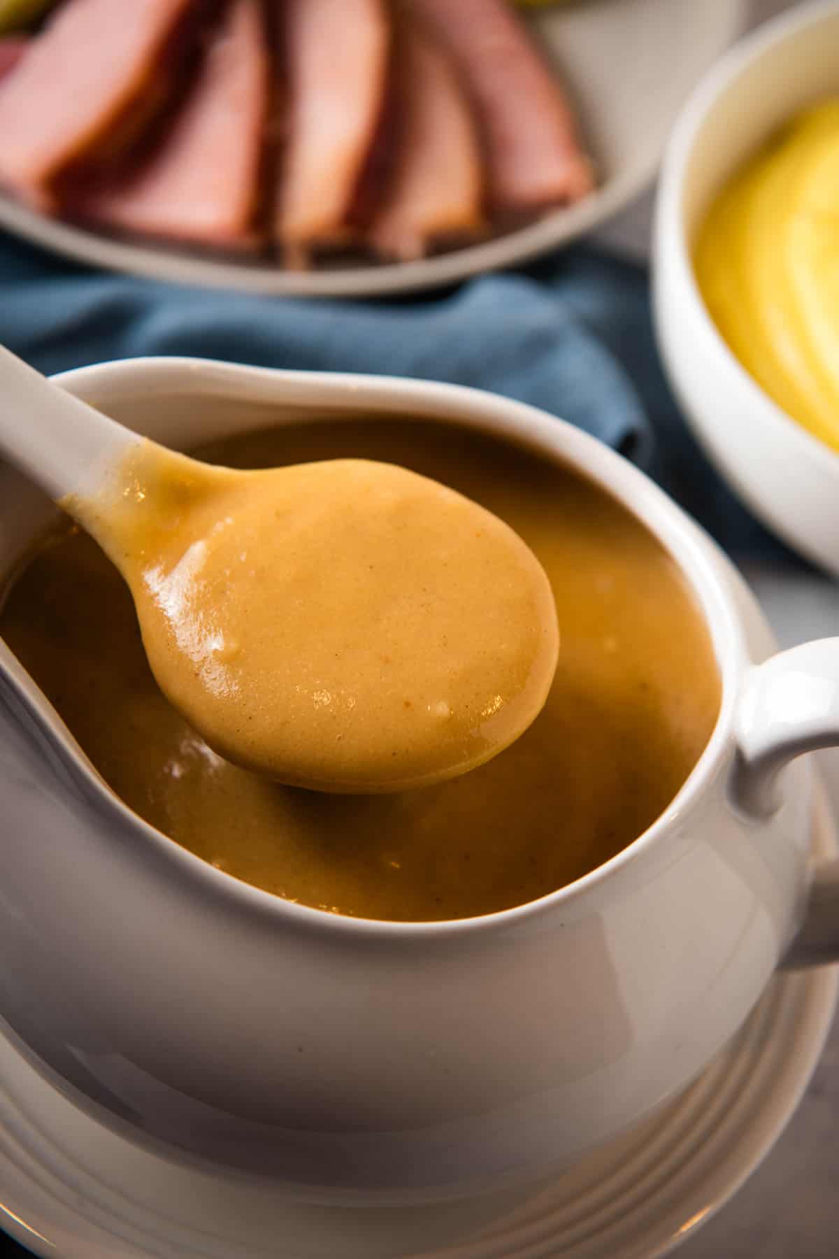 spoonful of homemade ham gravy over white gravy boat full of ham gravy