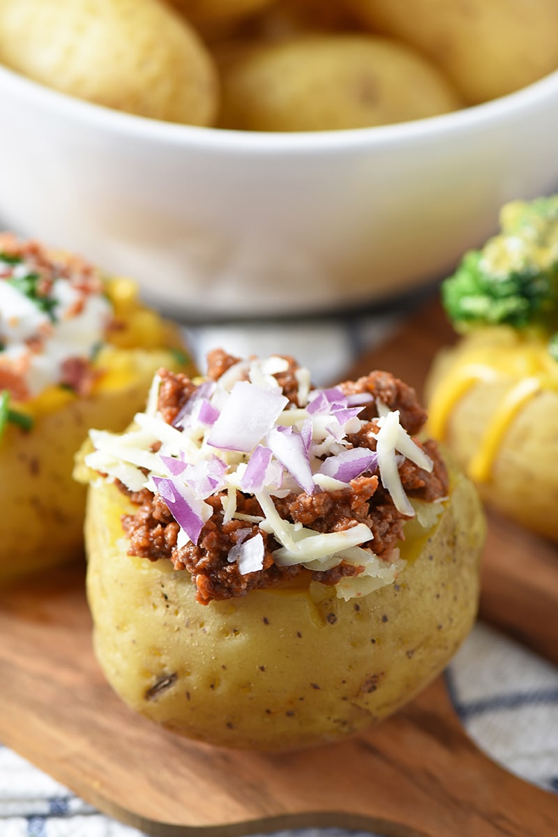 ultimate baked potato bar toppings, including sloppy joe ground beef, red onion, and shredded cheese, on wood cutting board