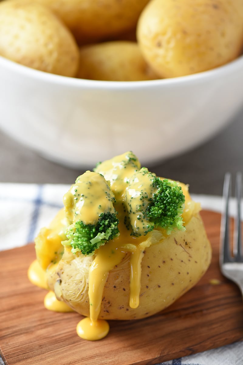 baked potato stuffed with broccoli and cheese sauce on wood cutting board