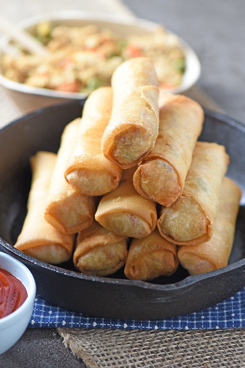 fried rice paper rolls stacked in cast iron skillet on blue cloth