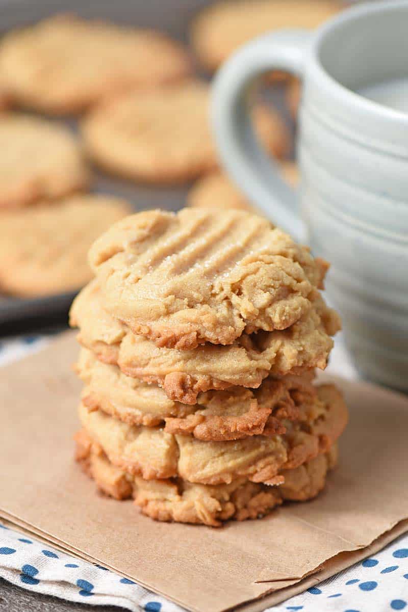 Stack of chewy peanut butter cookies on a brown paper bag with a cup of ice cold milk