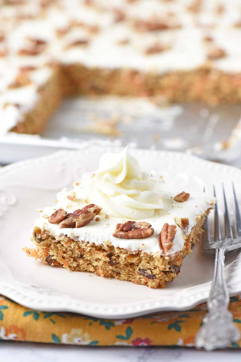 cream cheese frosting swirl on slice of carrot cake on white plate with fork