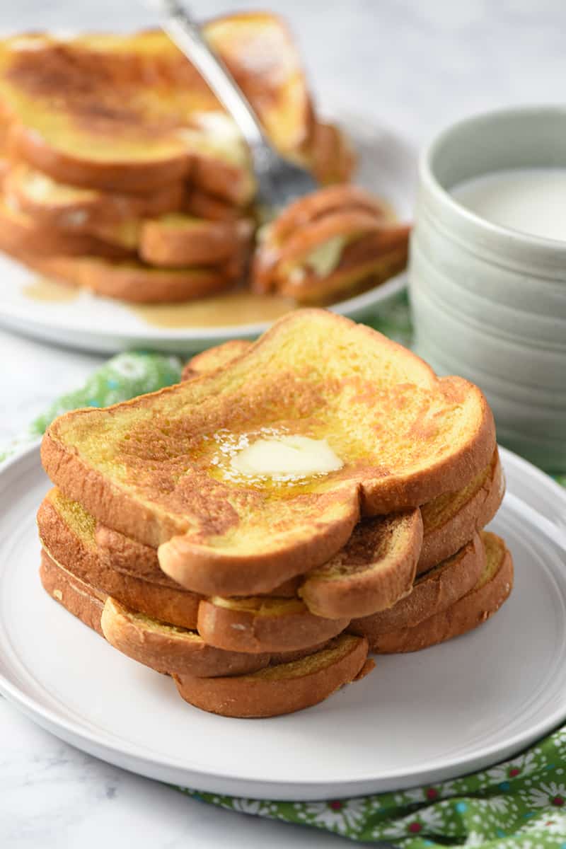 pile of French toast on plate with mug of milk