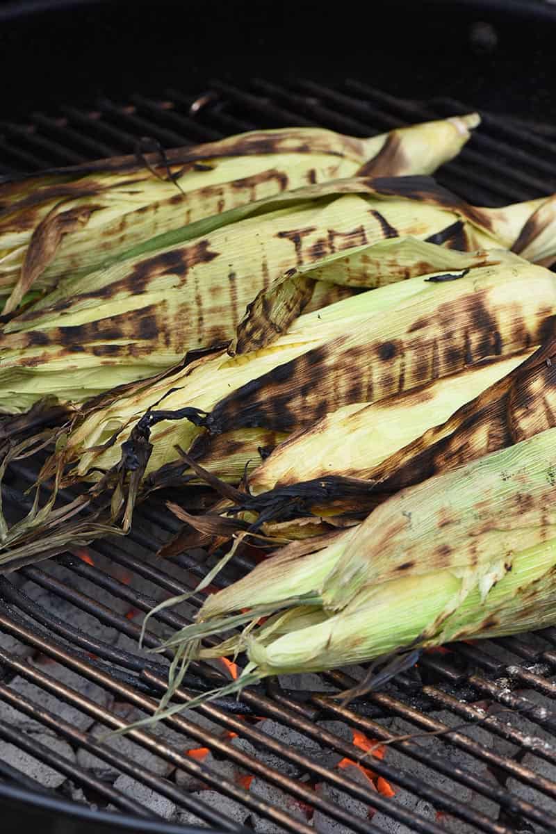 blackened grilled corn in the husk on a charcoal grill