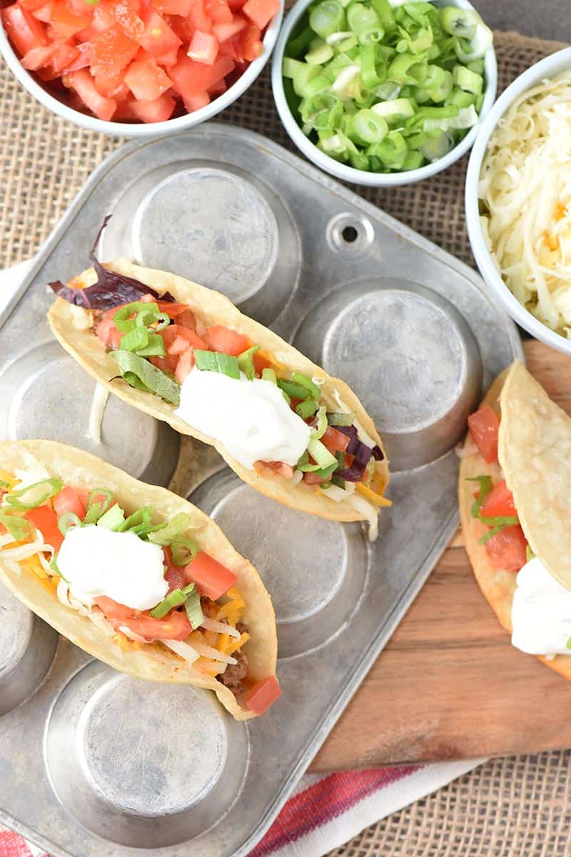 beef tacos in a muffin pan with all sorts of toppings ideas