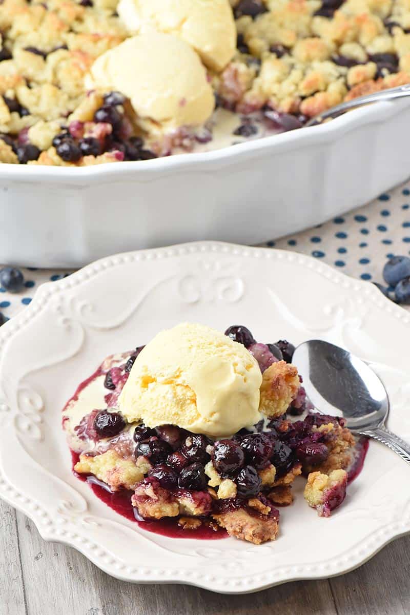 scoop of vanilla ice cream on top of homemade blueberry cobbler on a white plate
