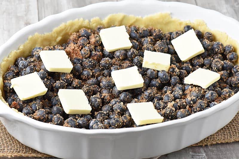 butter slices on top of blueberry cobbler in white baking dish