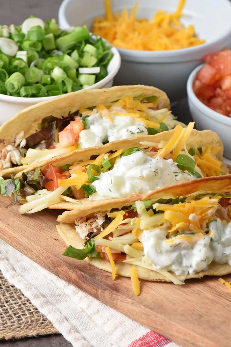 the best fish tacos ever with a tzatziki fish taco sauce on a wooden cutting board