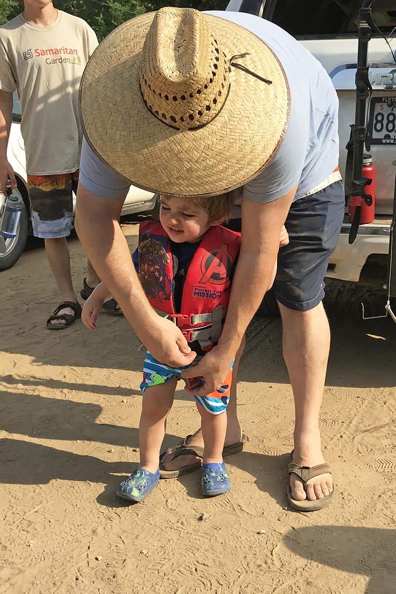dad putting life jacket on toddler before getting in kayak