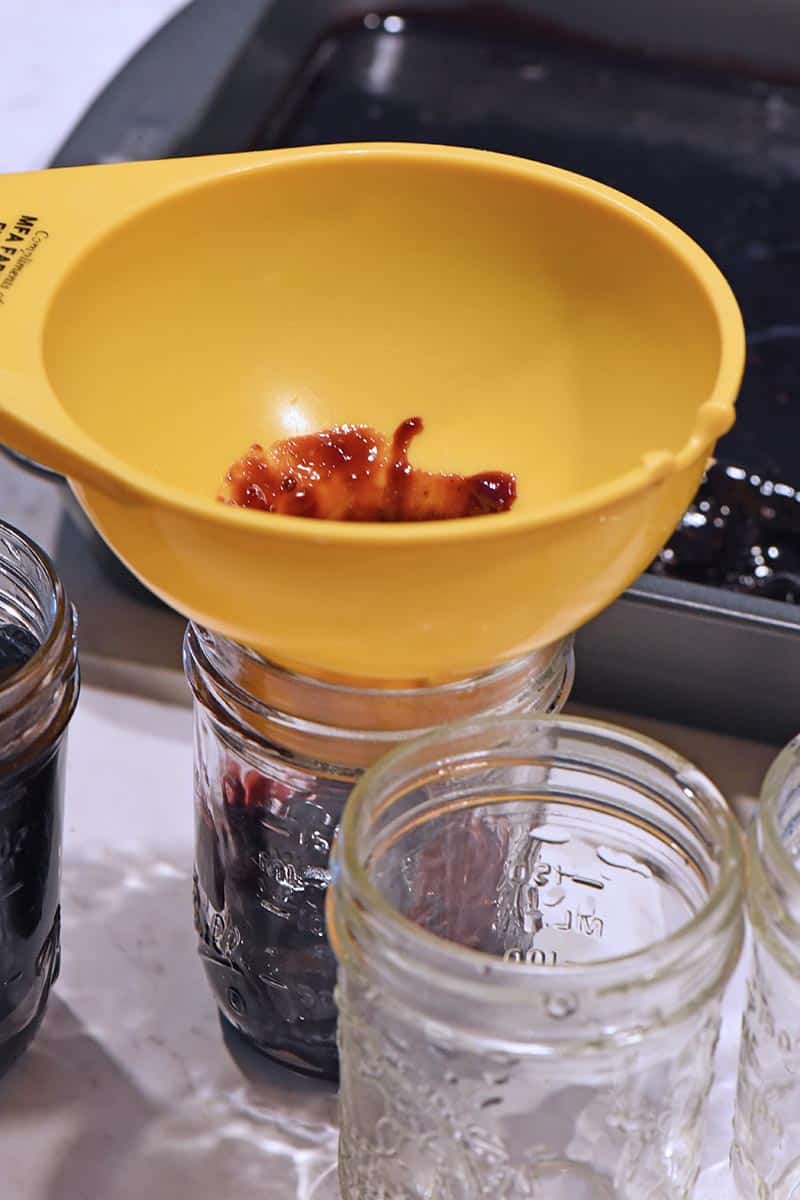 adding blackberry jam to jars with canning funnel