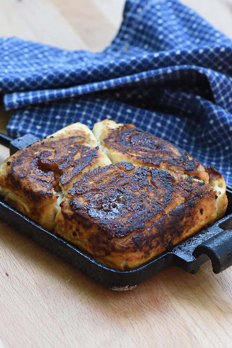 pie iron cinnamon rolls ready for icing, on wood cutting board with blue linen cloth