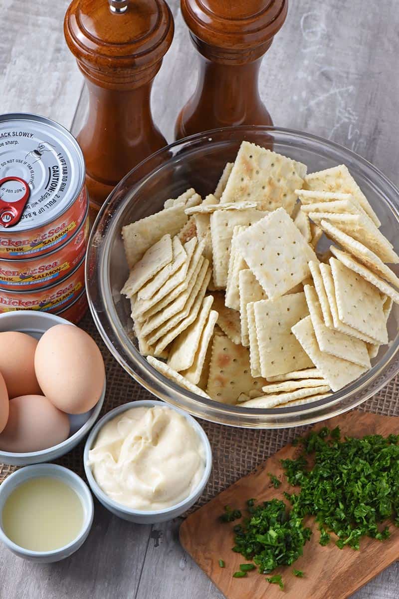 ingredients for salmon patties recipe, including canned salmon, Saltine crackers, lemon juice, eggs, fresh chives, fresh parsley, Miracle Whip, salt, and pepper