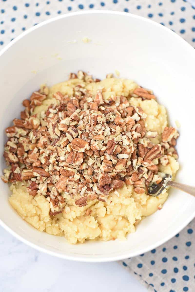 stirring pecans into homemade pie crust dough in white mixing bowl