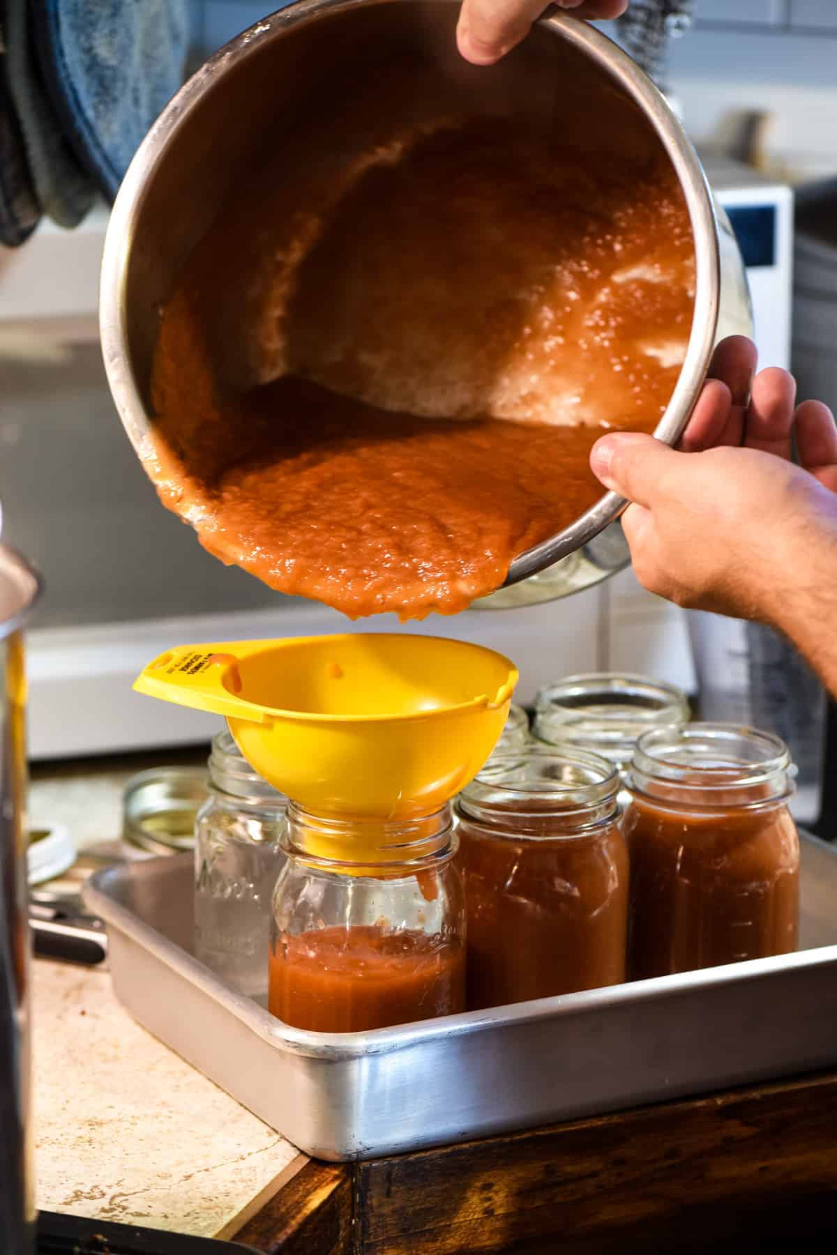 pouring homemade applesauce into canning jars with yellow canning funnel