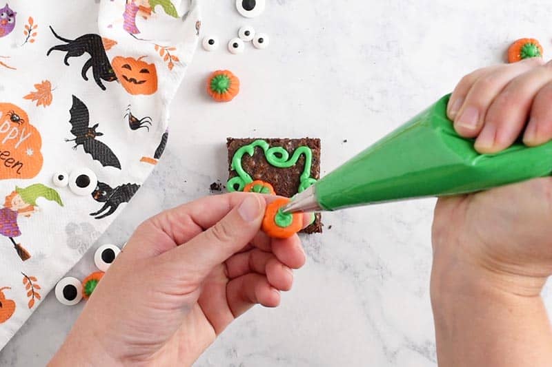 adding green icing to mellowcreme pumpkin for pumpkin patch Halloween brownies