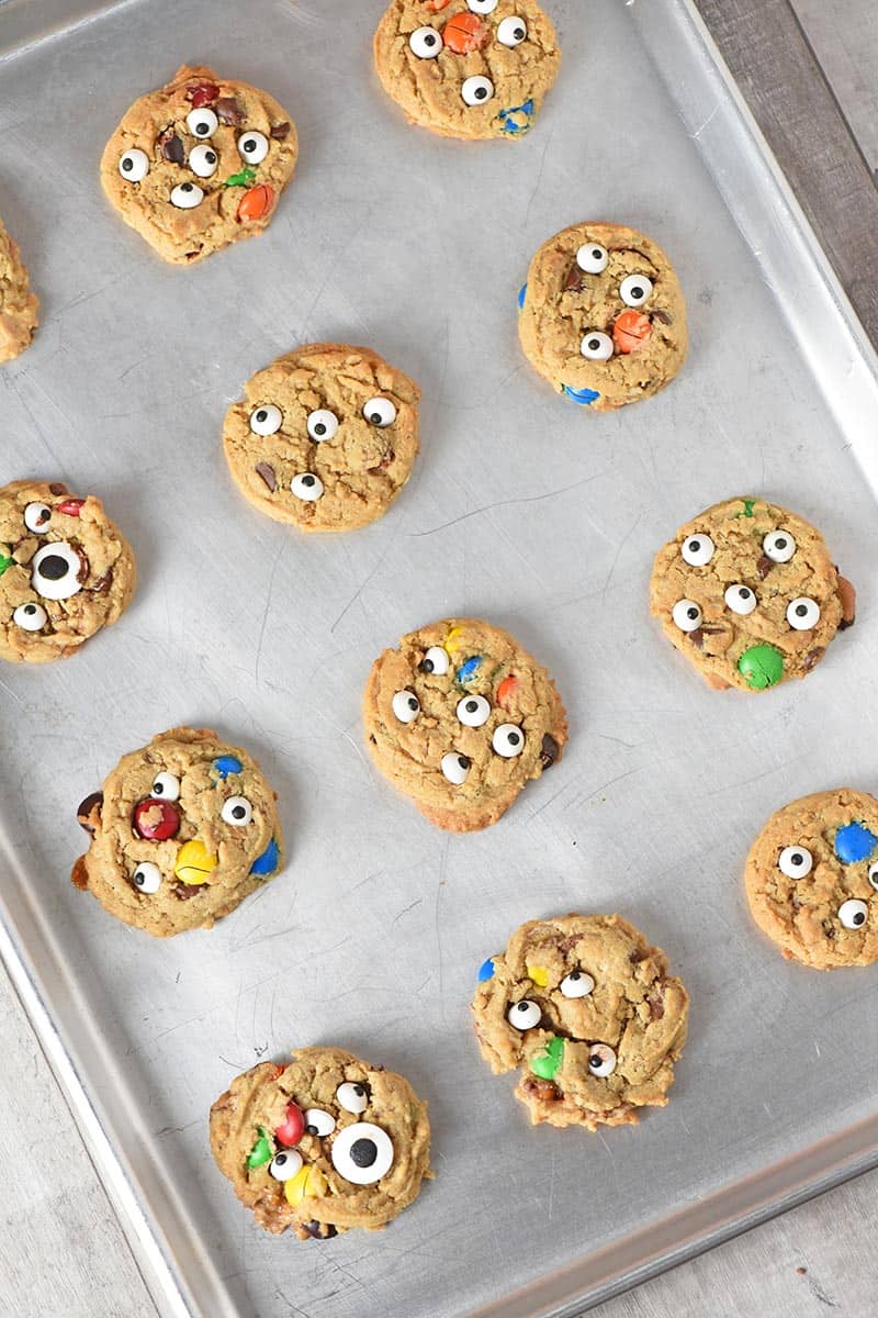 decorating Halloween cookies like monster cookies with candy eyeballs on a cookie sheet