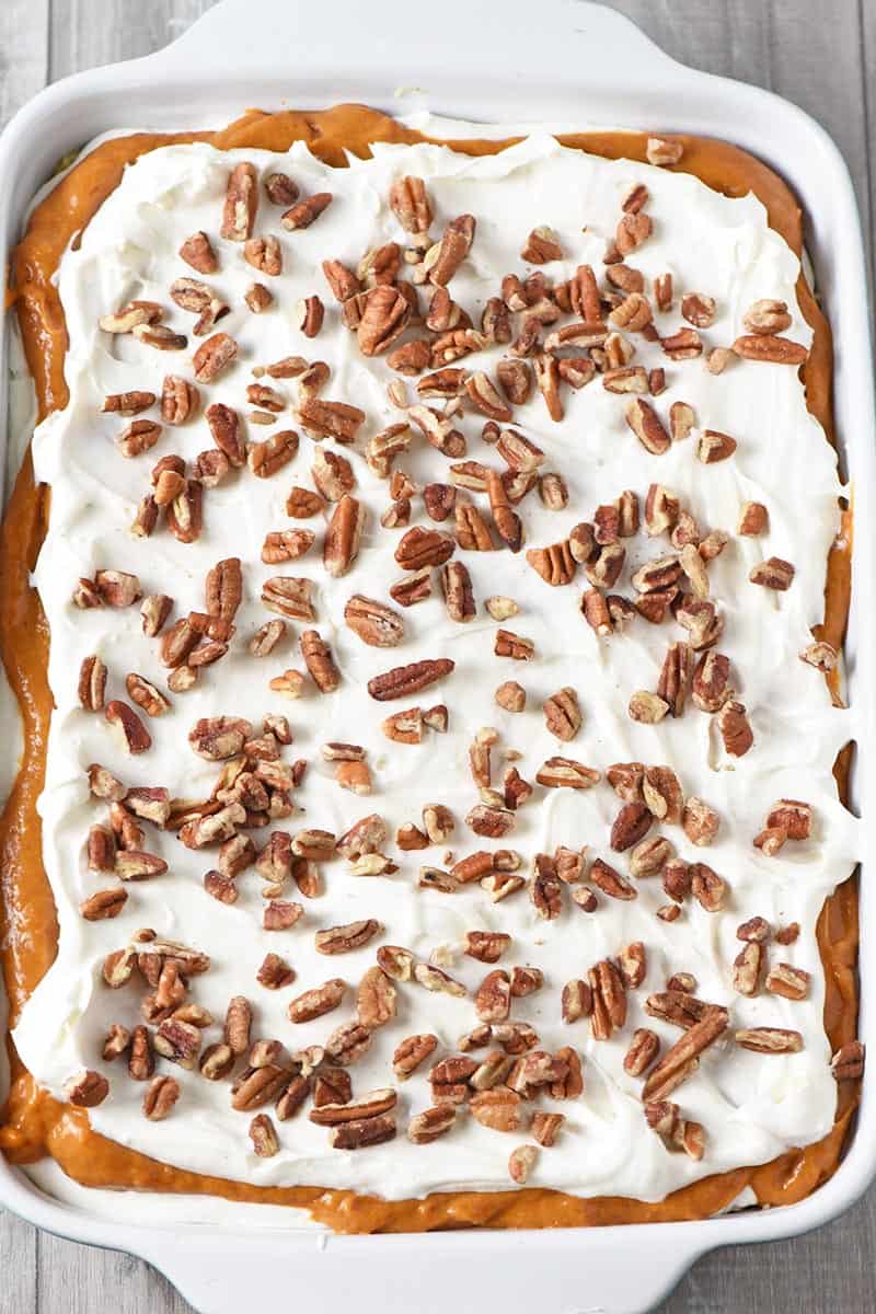 layered no bake pumpkin dessert recipe in blue baking dish with chopped pecans on top