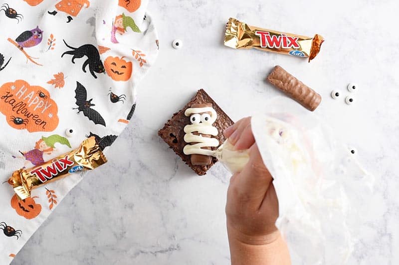wrapping mummy with icing from pastry bag on halloween brownies