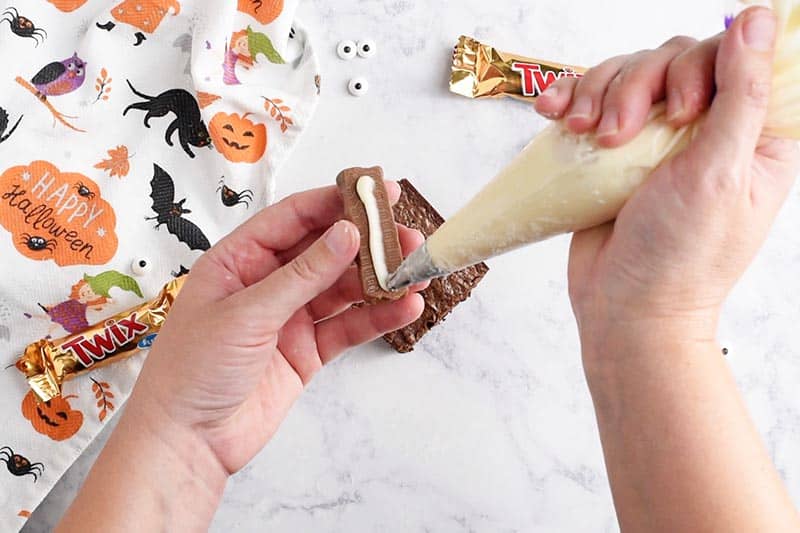 adding icing to back of Twix bar for mummy Halloween brownies