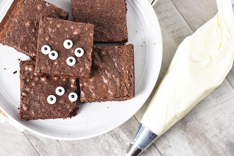 ingredients for ghost halloween brownies, including whipped cream, brownies, and candy eyeballs