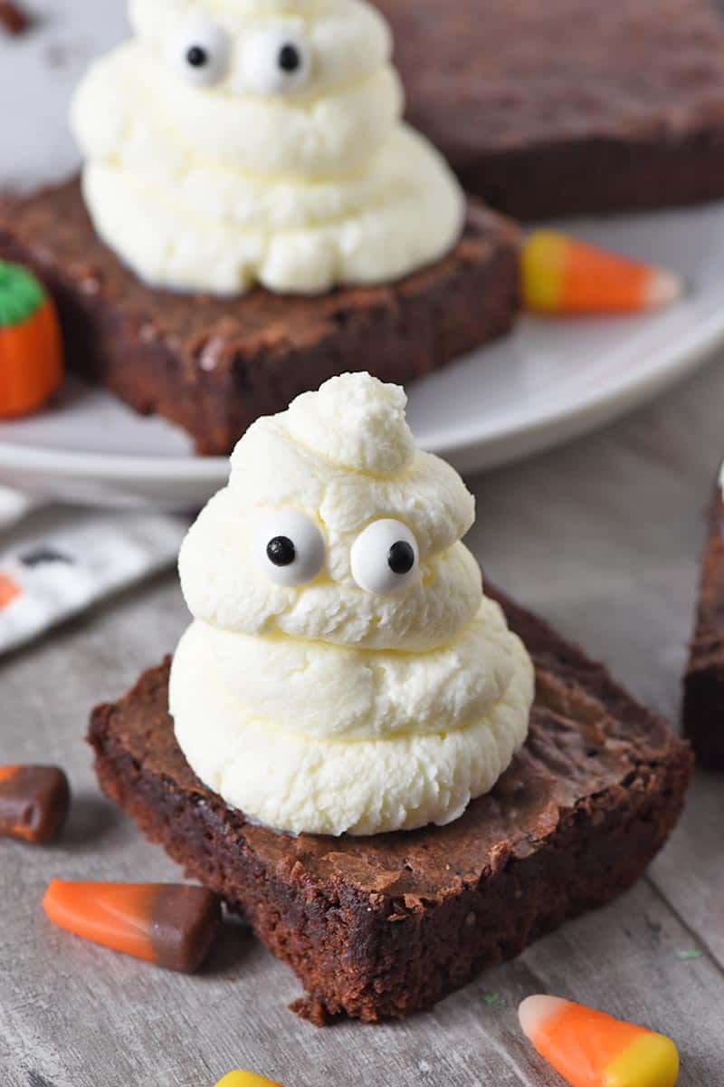 ghost halloween brownies made with whipped cream and candy eyeballs, on a countertop with candy corn and candy corn pumpkins