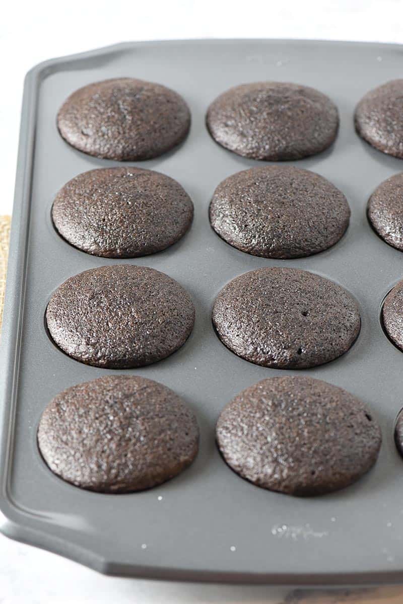 baked chocolate cupcakes in muffin pan on white marble countertop