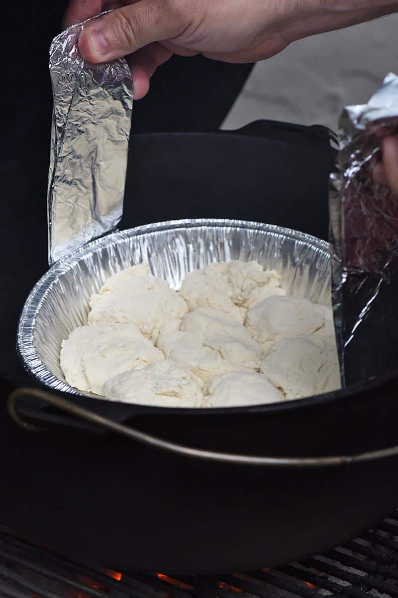 placing drop biscuits down into Dutch oven with tin foil sling for baking over a campfire