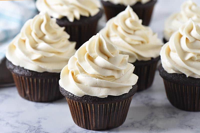 homemade chocolate cupcakes with a blue striped towel on a white marble countertop